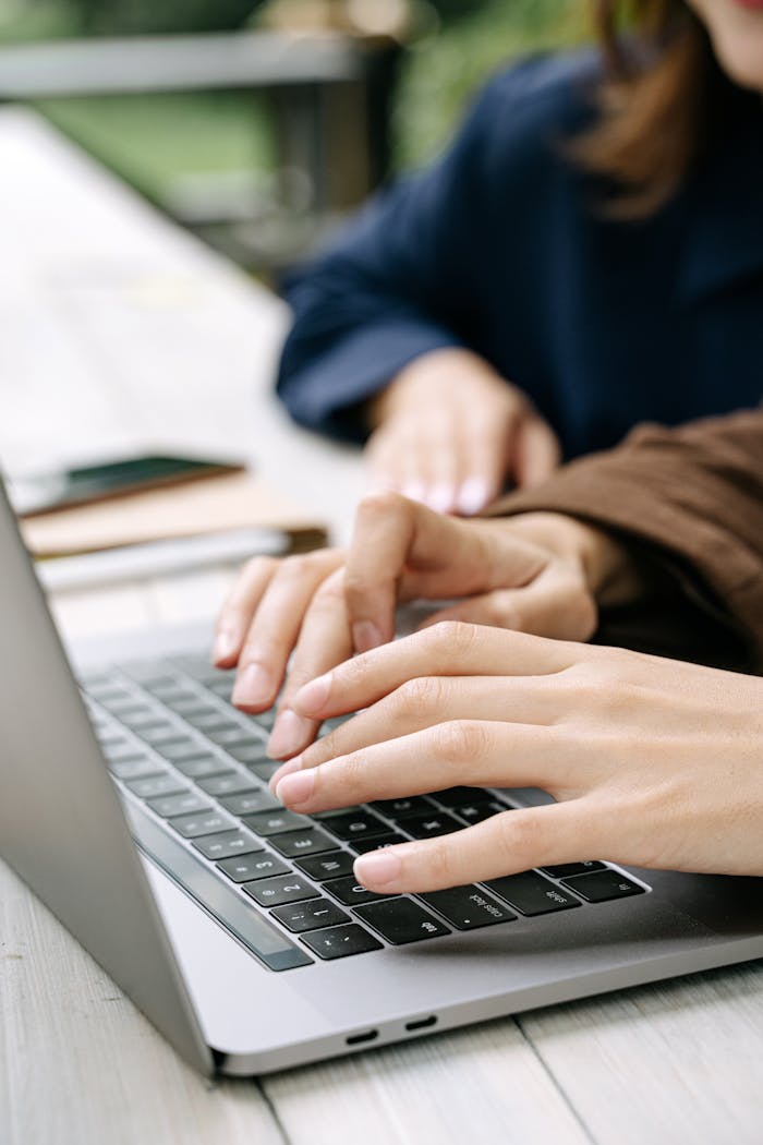 Close-up of hands typing on a laptop outdoors, emphasizing teamwork and technology.